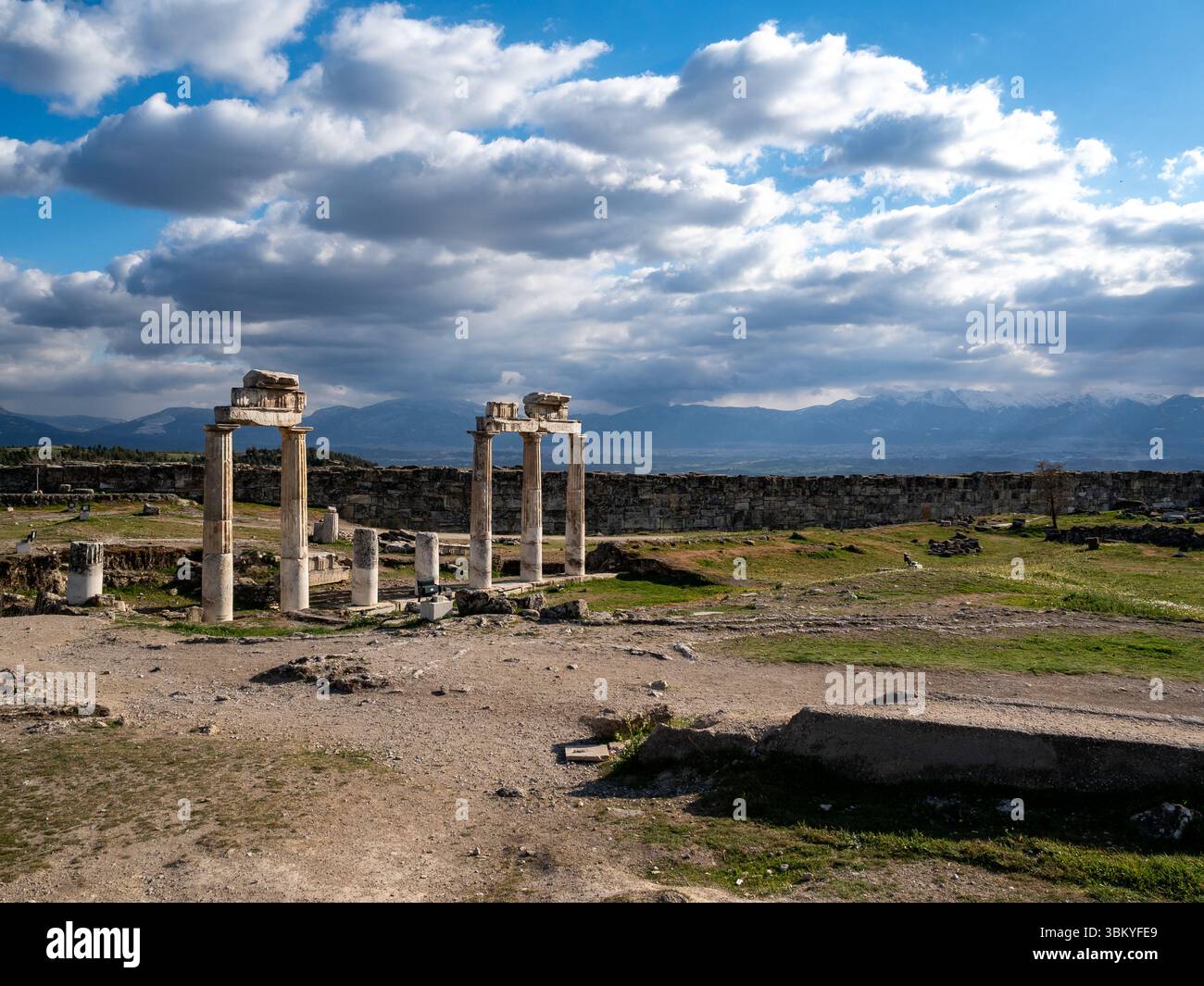 L'image montre les ruines de Hiérapolis, une ancienne ville située près de Pamukkale en Turquie. Les ruines comprennent des colonnes et des murs, et le paysage environnant est un mélange de terre, d'herbe et de montagnes. Le ciel est nuageux, et la scène globale est une scène d'importance historique et de beauté naturelle. Banque D'Images L'image montre les ruines de Hiérapolis, une ancienne ville située près de Pamukkale en Turquie. Les ruines comprennent des colonnes et des murs, et le paysage environnant est un mélange de terre, d'herbe et de montagnes. Le ciel est nuageux, et la scène globale est une scène d'importance historique et de beauté naturelle. Banque D'Images