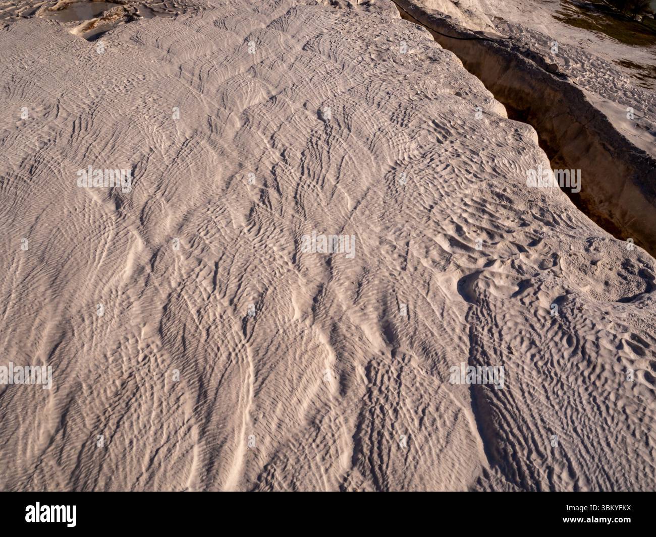 Une vue aérienne capture les motifs complexes gravés dans les terrasses de travertin blanc de Pamukkale, en Turquie, mettant en valeur la merveille naturelle formée par les eaux thermales riches en minéraux. Banque D'Images