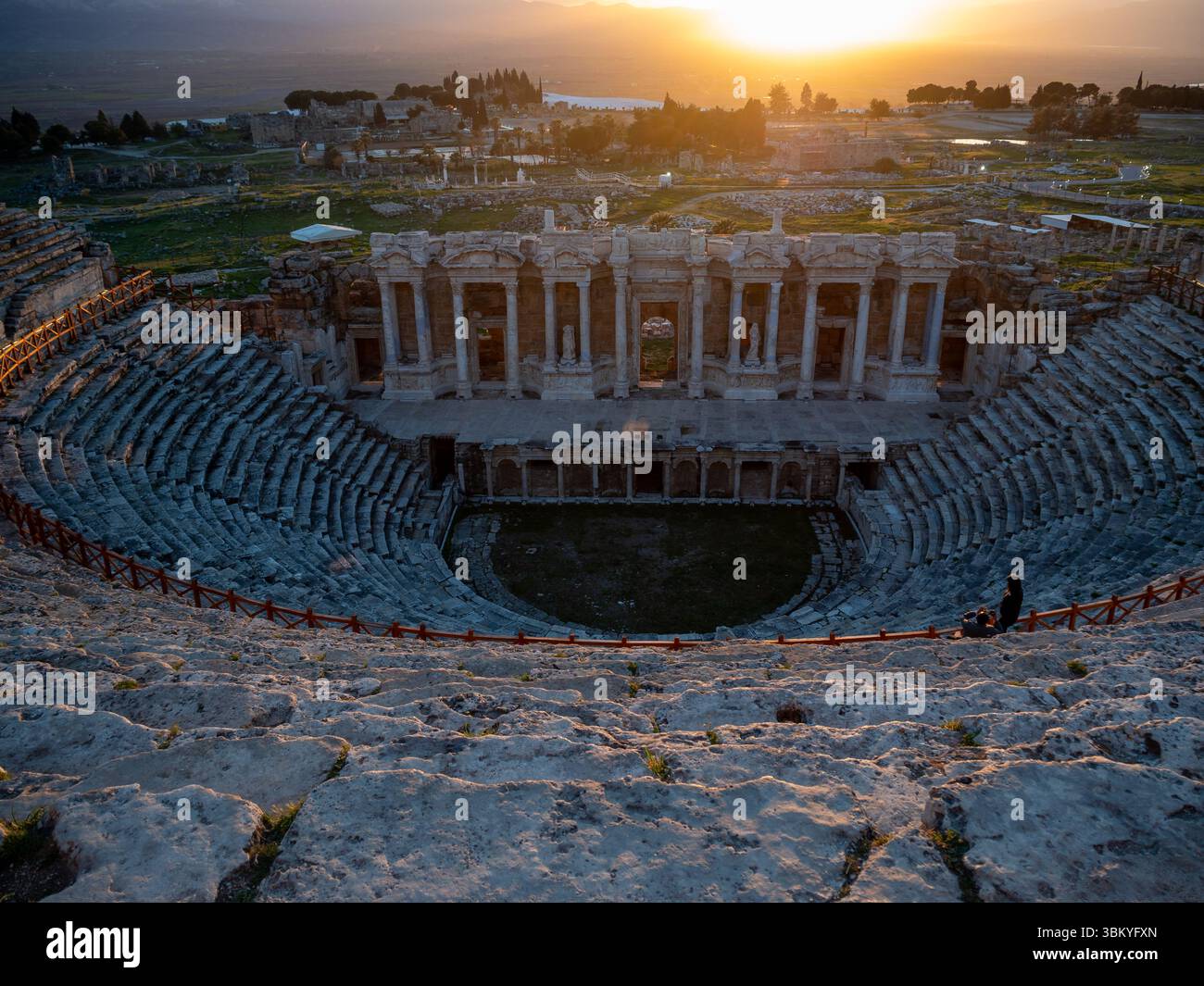 Deux personnes sont debout sur les marches du théâtre antique de Hiérapolis, en Turquie, en admirant la vue sur les ruines et le coucher du soleil. Banque D'Images Deux personnes sont debout sur les marches du théâtre antique de Hiérapolis, en Turquie, en admirant la vue sur les ruines et le coucher du soleil. Banque D'Images