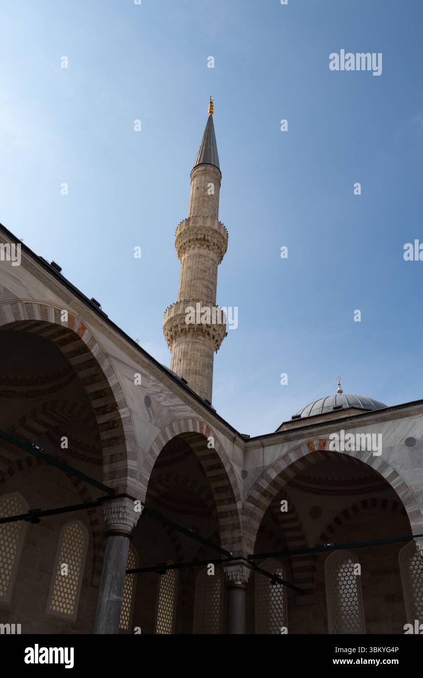 Une prise de vue en angle bas capture les détails architecturaux d'une mosquée, mettant en valeur son minaret, ses arches et son dôme contre un ciel bleu clair. Banque D'Images