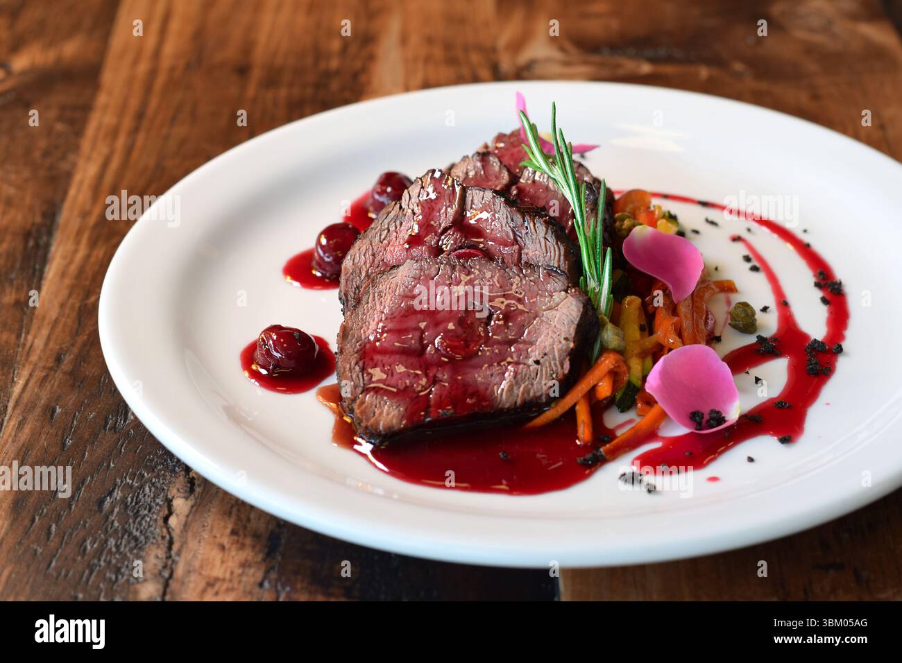 Tranches de veau cuit servies avec julienne de légumes et sauce cerise, garni de brin de romarin Banque D'Images