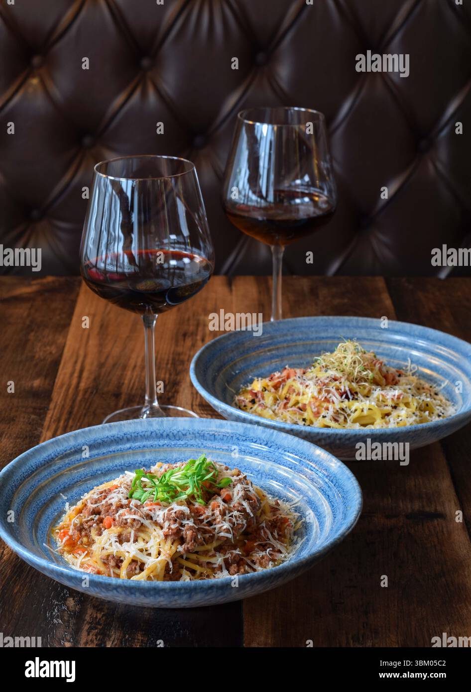 Deux bols de pâtes et deux verres de vin rouge sur une table en bois Banque D'Images
