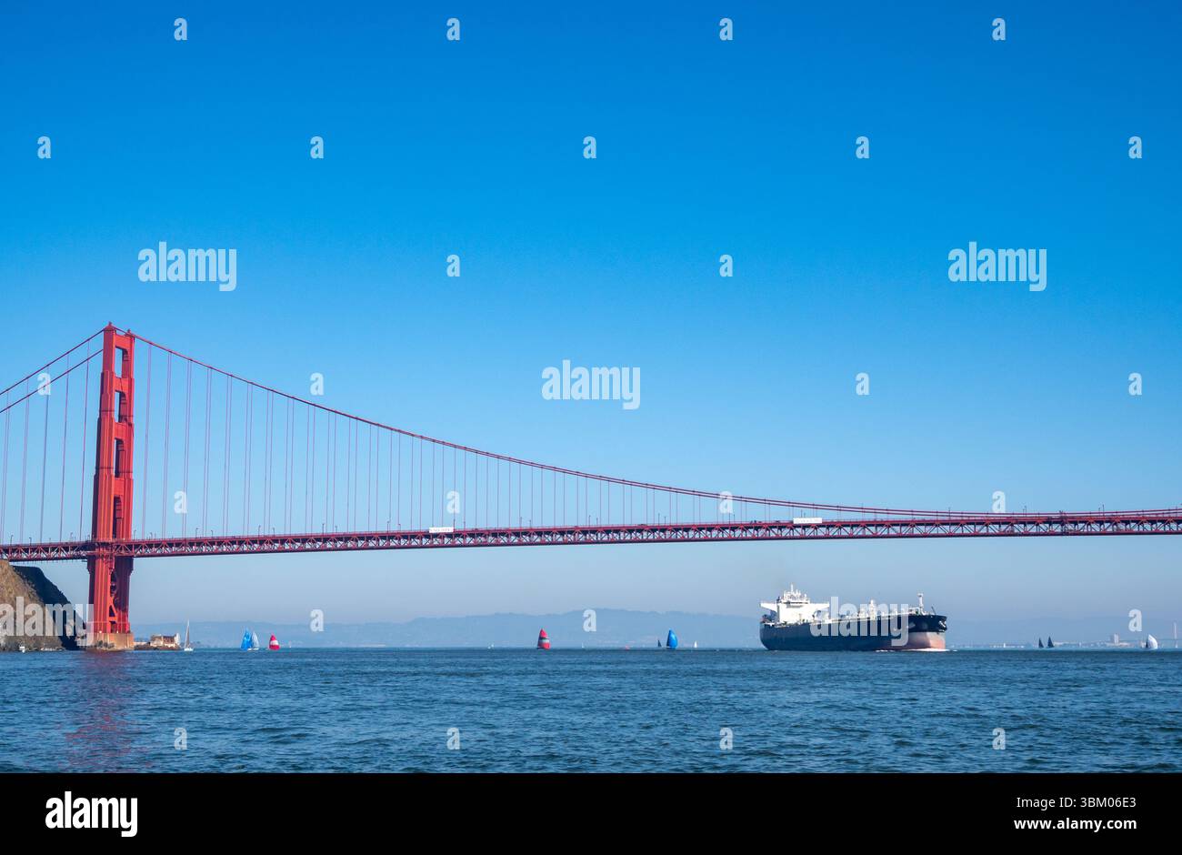 Un grand cargo navigue sous le Golden Gate Bridge, tandis que des voiliers sont également sur l'eau. Banque D'Images