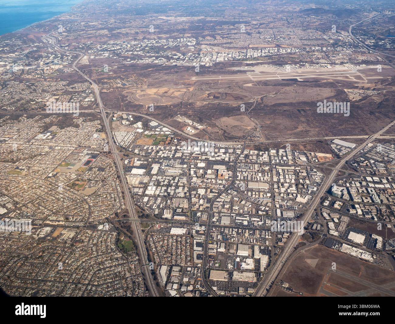 Une vue aérienne montre l'étalement urbain d'une ville, avec des zones résidentielles, des bâtiments commerciaux et des infrastructures de transport, y compris des autoroutes et un aéroport, illustrant l'organisation complexe et le développement des environnements urbains modernes. Banque D'Images