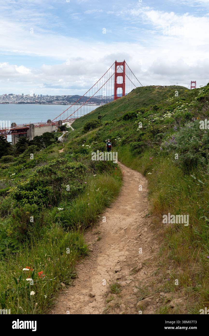 Un randonneur marche le long d'un chemin de terre sur une colline, avec le Golden Gate Bridge en arrière-plan, profitant du paysage et de l'exercice. Banque D'Images Un randonneur marche le long d'un chemin de terre sur une colline, avec le Golden Gate Bridge en arrière-plan, profitant du paysage et de l'exercice. Banque D'Images