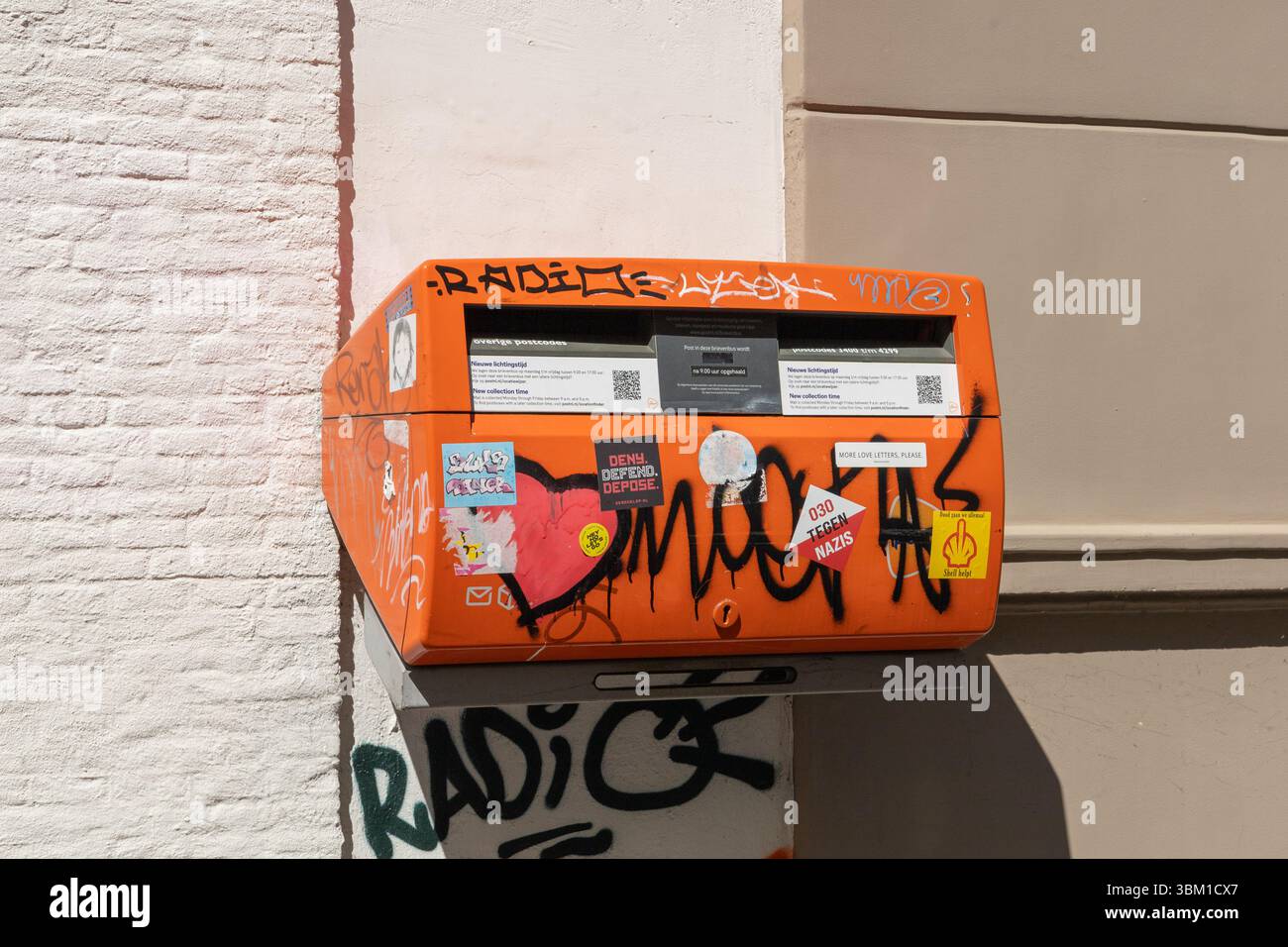 Une boîte aux lettres hollandaise orange à Nieuwegein, Utrecht, recouverte de graffitis et d'autocollants, attachée à un bâtiment avec des murs de briques et de stuc Utrecht, le Neth Banque D'Images