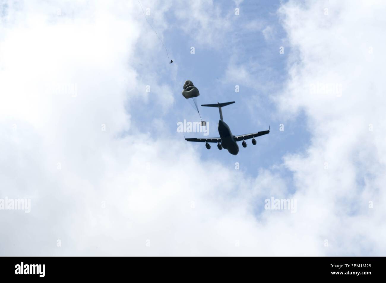 Un C-17 Globemaster III de l'US Air Force dépose une cargaison à Kanes Drop zone sur Oahu, le 18 juin 2025. Le 535e escadron de transport aérien organise une formation hebdomadaire au largage de fret pour assurer la préparation à la mission pour de futures opérations dans le monde réel partout dans le monde. (Photo américaine du sergent d'état-major Alan Ricker) Banque D'Images