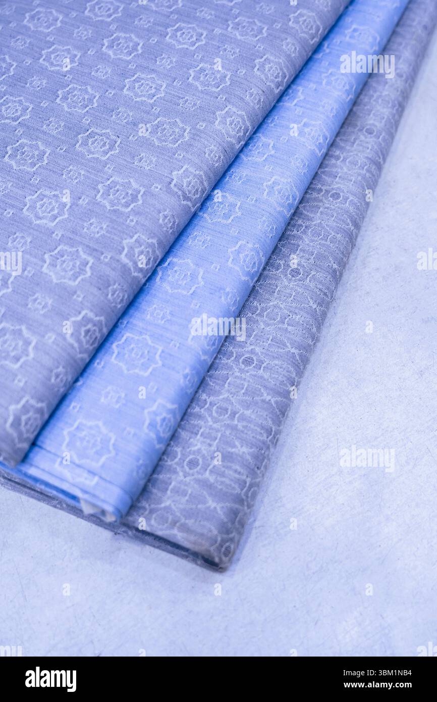 L'image montre trois morceaux pliés de tissu à motifs dans les tons de bleu et de gris. Les textiles arborent un subtil motif floral en relief. Banque D'Images