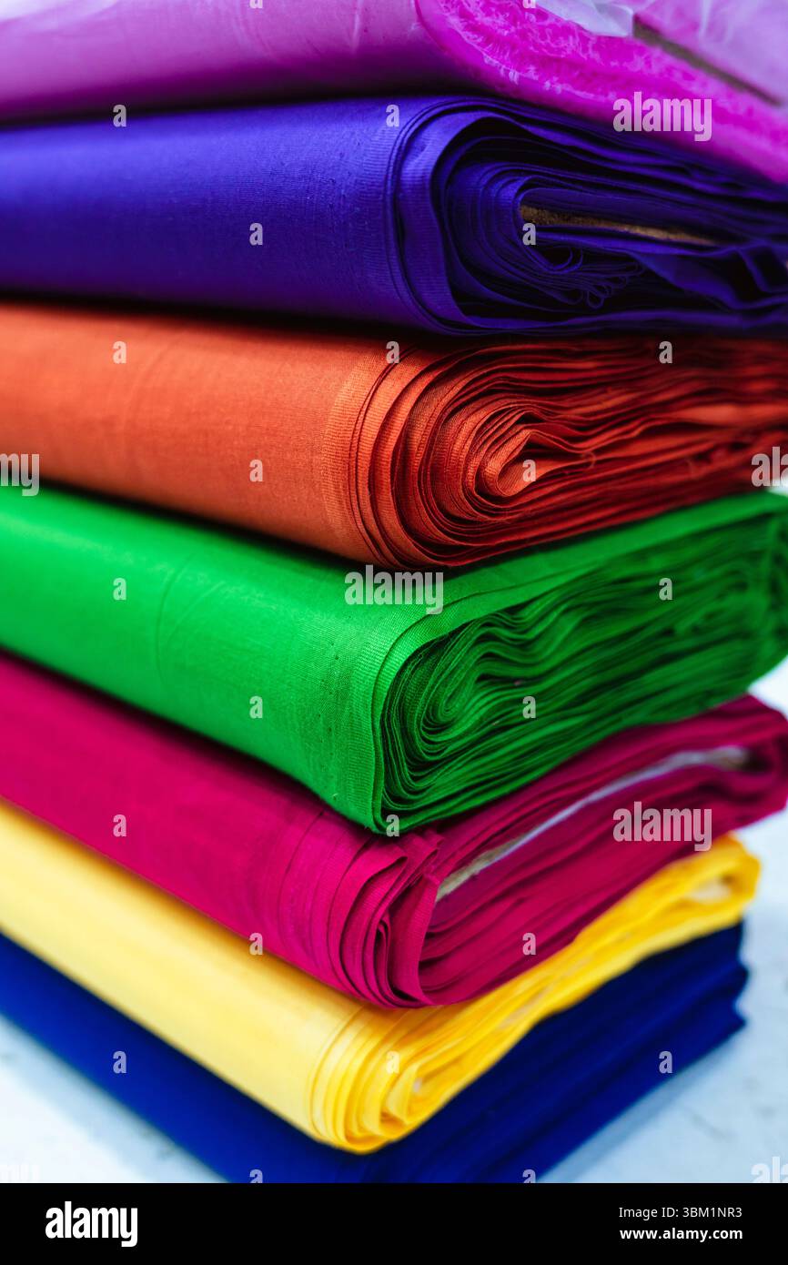 Vue rapprochée d'une pile de tissus roulés présentant une variété de couleurs riches, y compris violet, bleu, orange, vert, rose, jaune et bleu. L'ambiance Banque D'Images