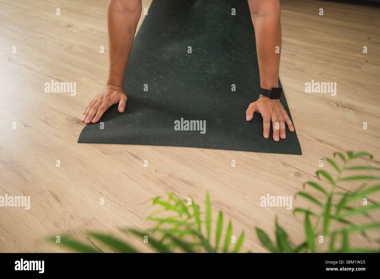 Gros plan de mains masculines adultes tenant une pose de planche statique sur un tapis de yoga vert foncé lors d'une séance d'entraînement à la maison sur un parquet clair Banque D'Images
