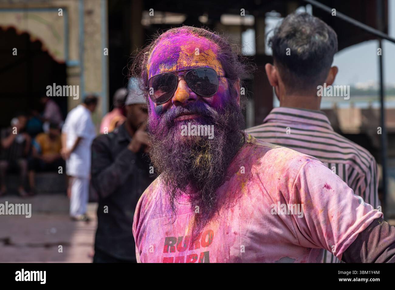 Inde, Jaipur, 22 mars 2025. Homme barbu couvert de poudre colorée pendant les célébrations du festival Holi à Jaipur. Portrait de rue avec lunettes de soleil Banque D'Images