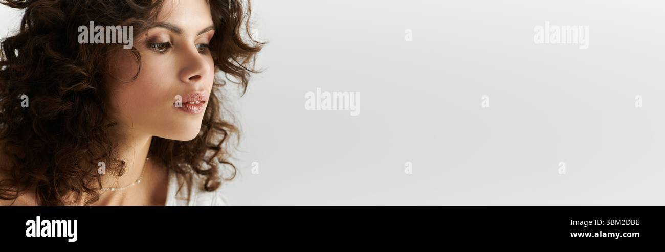 Jeune femme aux cheveux bouclés affiche sa tenue élégante et son expression confiante dans une ambiance sereine. Banque D'Images