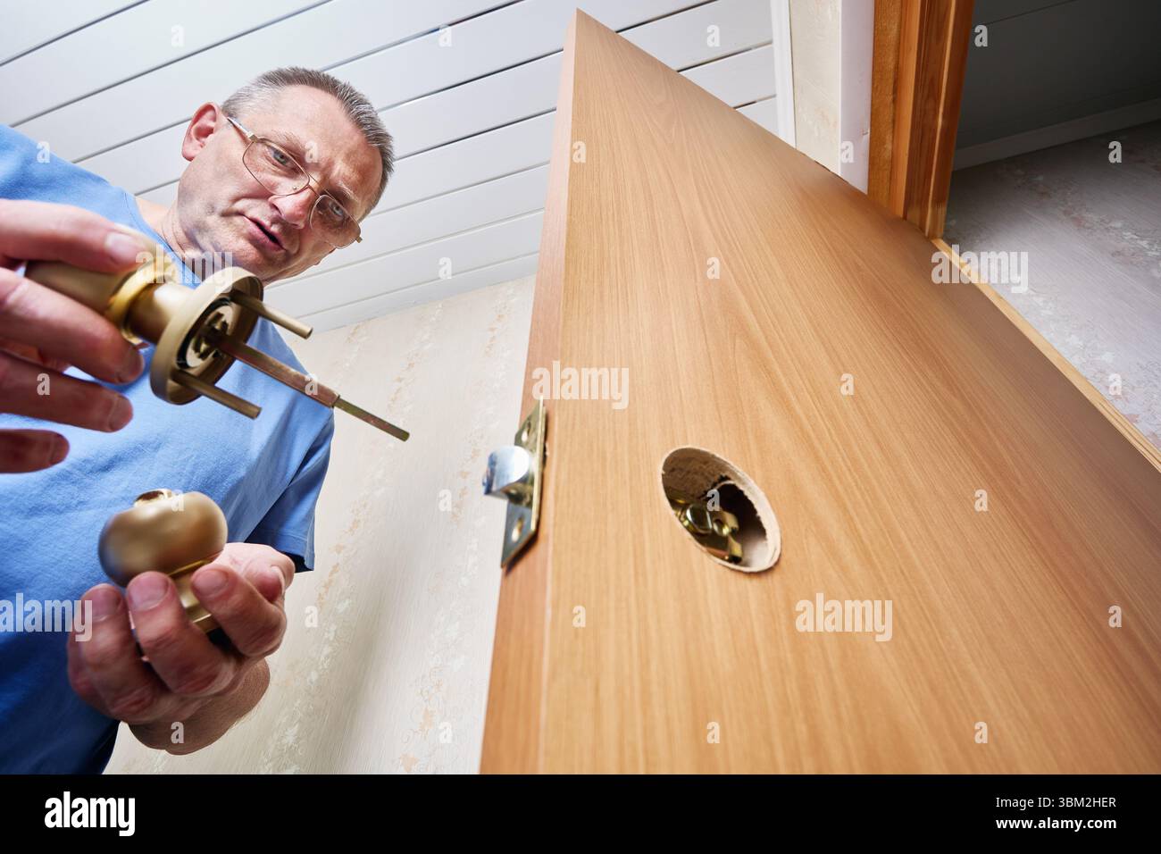 Serrurier se préparant à insérer l'ensemble de bouton de porte dans le trou prépercé de la porte en bois pour terminer l'installation et assurer le bon fonctionnement du verrouillage Banque D'Images