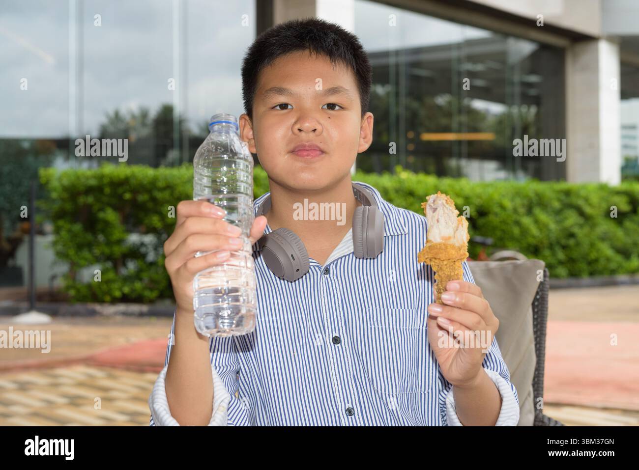 Garçon étudiant thaïlandais mangeant du poulet frit et buvant de l'eau à l'extérieur Banque D'Images
