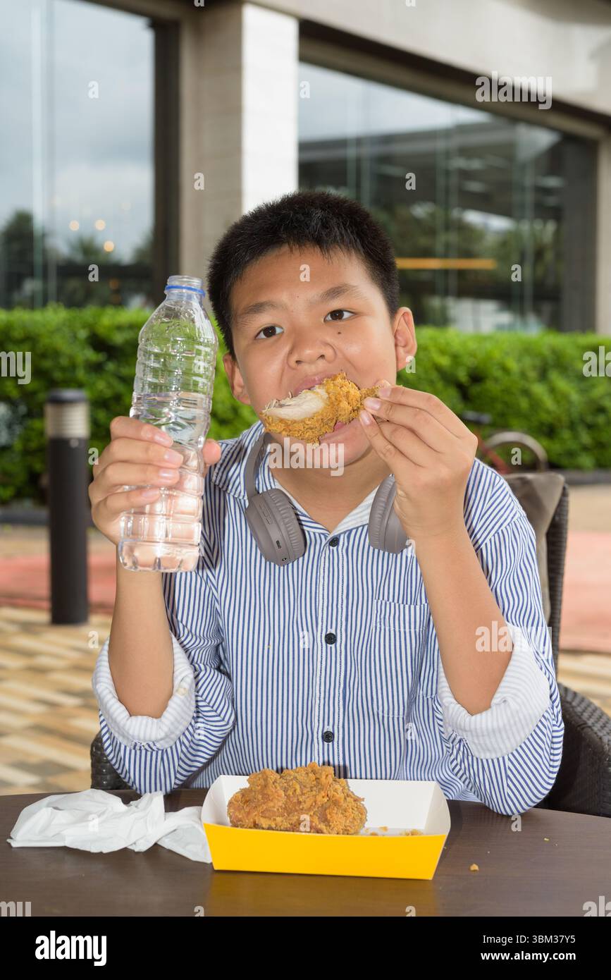 Garçon étudiant thaïlandais mangeant du poulet frit et buvant de l'eau à l'extérieur Banque D'Images