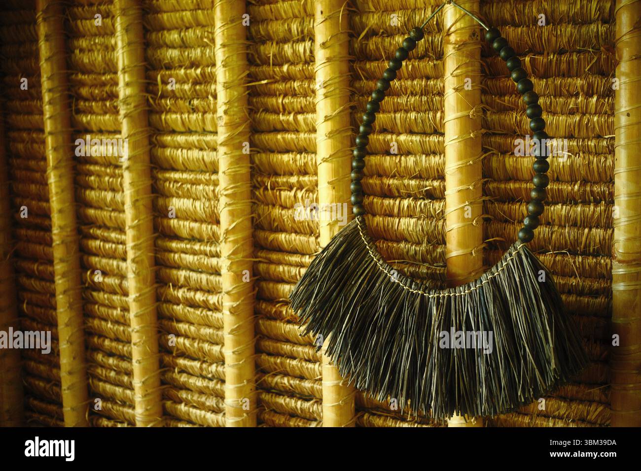 Un collier décoratif de style tribal avec des perles en bois et une frange de fibre naturelle accrochée au mur d'une cabane en bambou tissé Banque D'Images