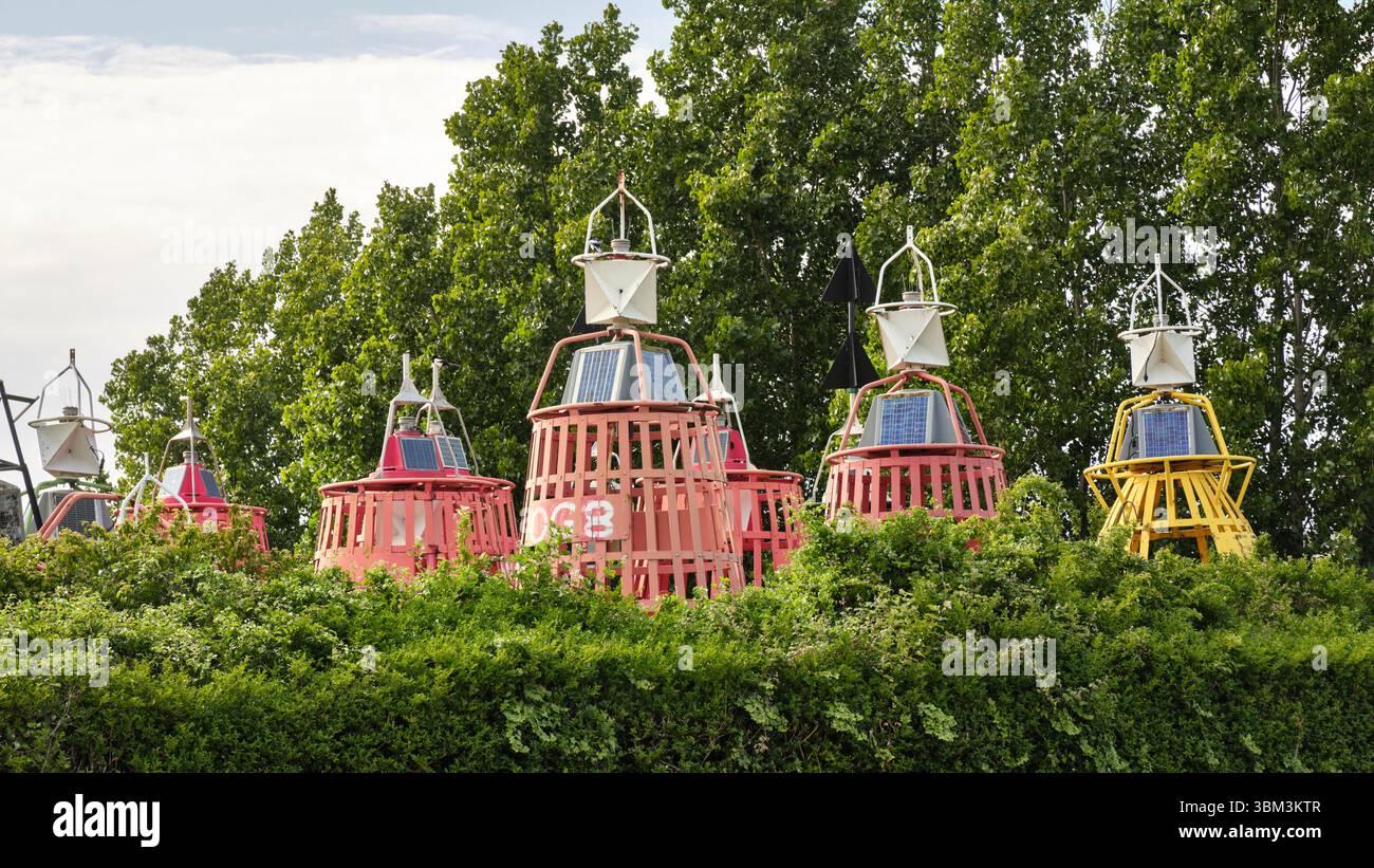 28 mai 2025 - Vlissingen-pays-Bas : rangée de bouées de navigation maritime colorées avec des panneaux solaires sur le dessus, partiellement visible au-dessus d'une haie verte au th Banque D'Images