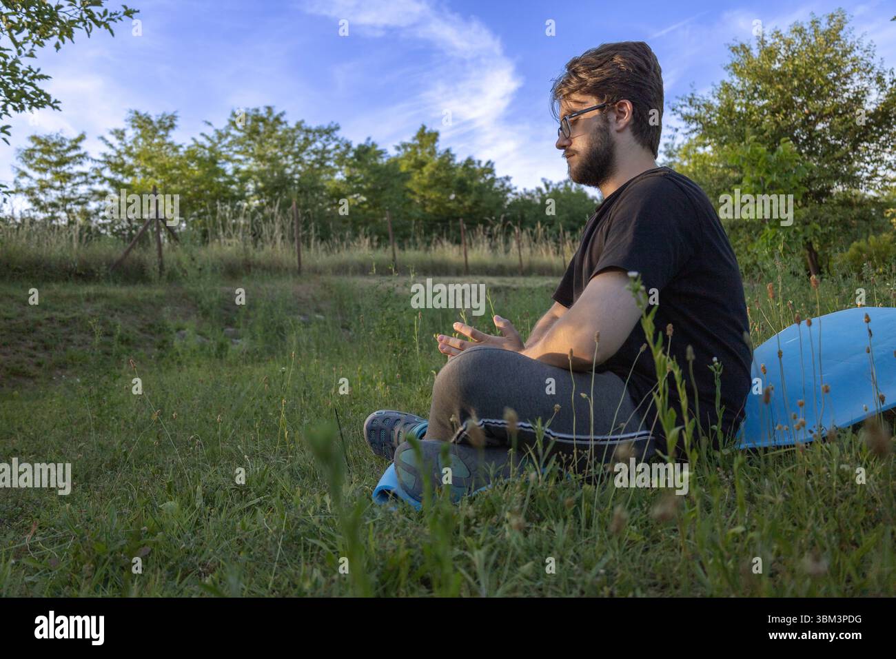 Vue latérale de l'homme méditant paisiblement dans l'herbe Banque D'Images