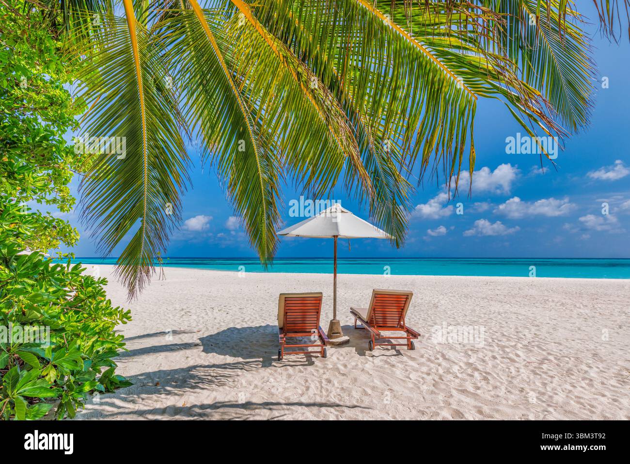 Belle plage romantique chaises de loisirs parasol sous le ciel ensoleillé, couple d'amour destination lune de miel paysage tropical pour des vacances reposantes Banque D'Images