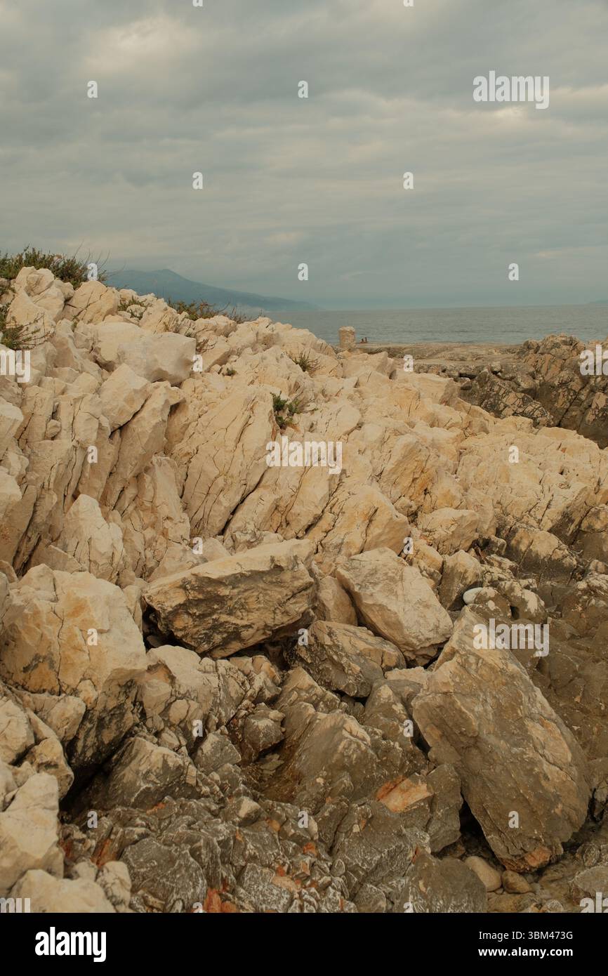 Rochers côtiers déchiquetés sous un ciel couvert par la mer Adriatique. Les tons terreux et les textures de pierre fracturée dominent le premier plan. Banque D'Images