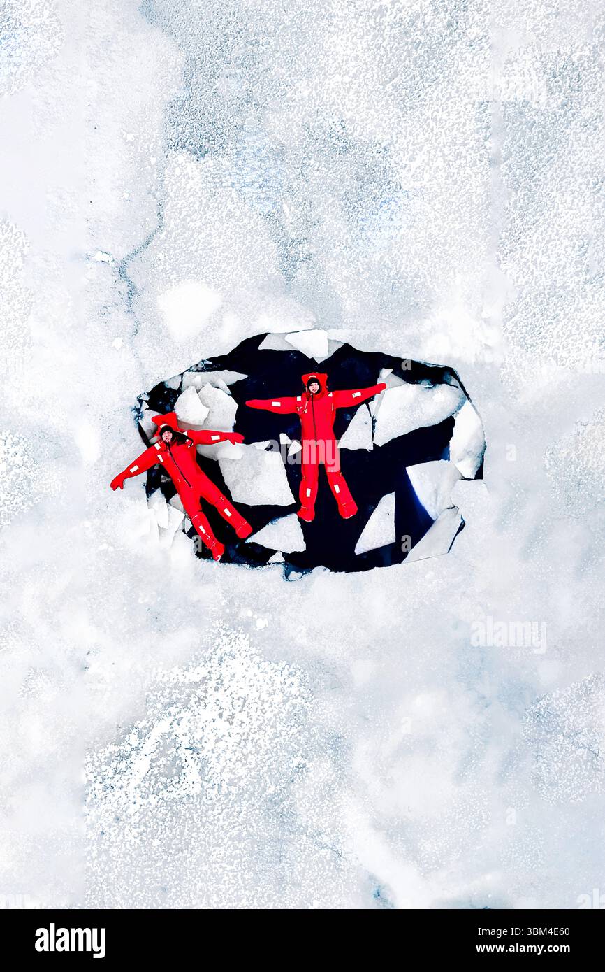 Vue aérienne de deux personnes de glace flottant sur l'eau glacée dans des combinaisons de survie rouge vif. Paysage glacé arctique. Aventure extrême, plongée sous glace, eau froide s Banque D'Images