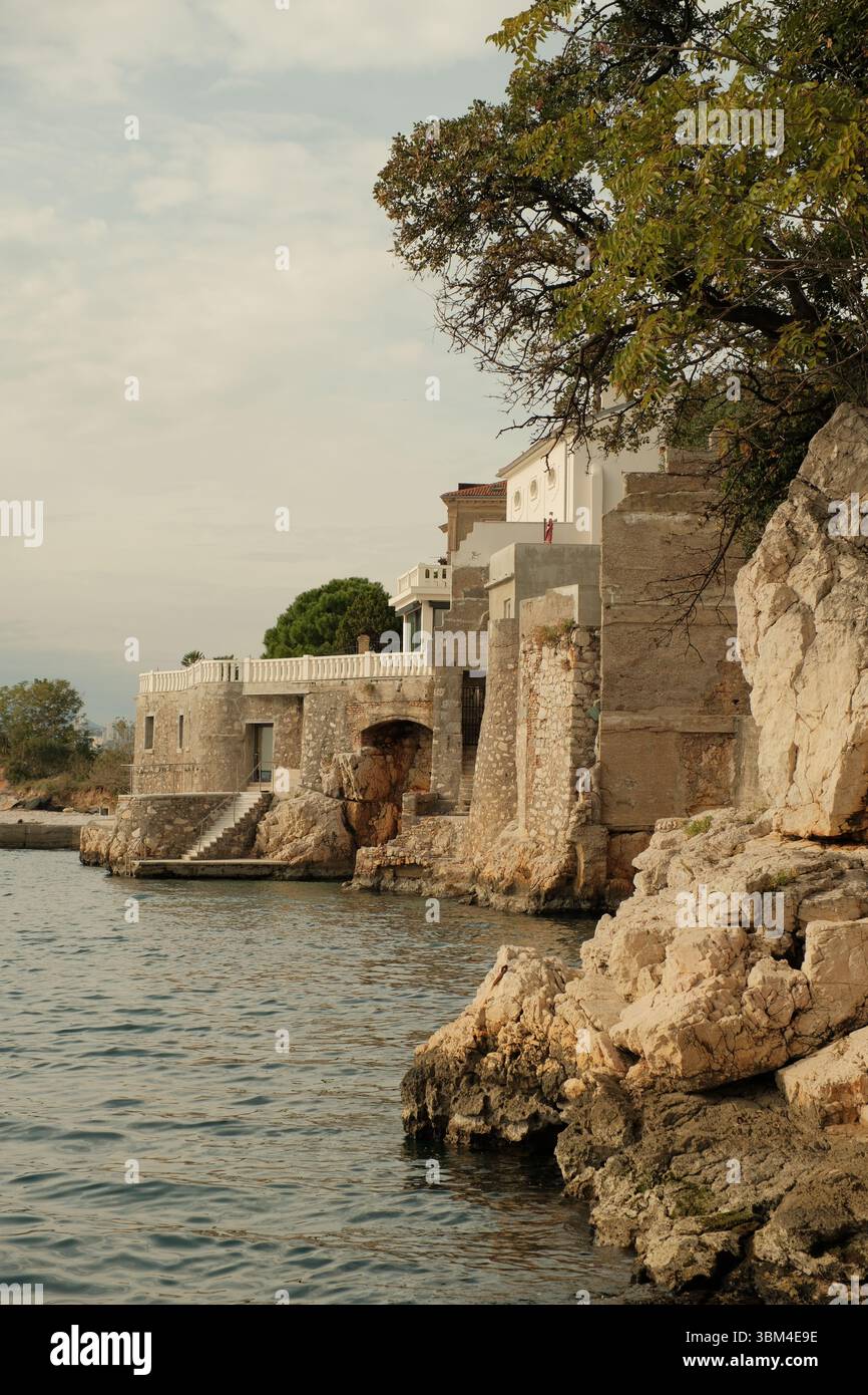 Les bâtiments en pierre se dressent de manière résiliente sur la côte croate accidentée, leurs façades altérées se mélangeant avec les roches calcaires naturelles dont ils émergent. Banque D'Images