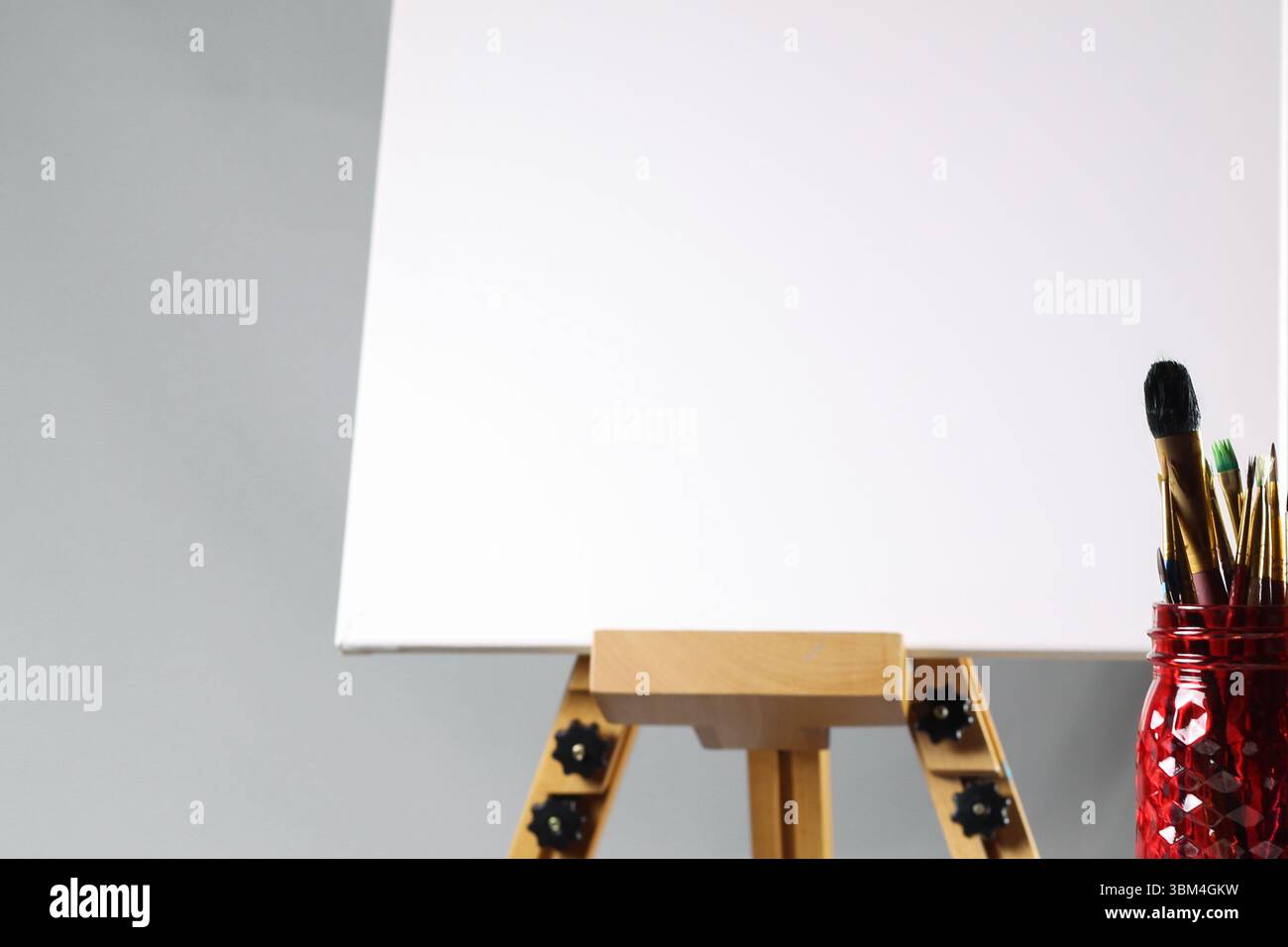 Red Mason pot de pinceaux devant Blank Canvas – Artistic Workspace Still Life Banque D'Images Red Mason pot de pinceaux devant Blank Canvas – Artistic Workspace Still Life Banque D'Images
