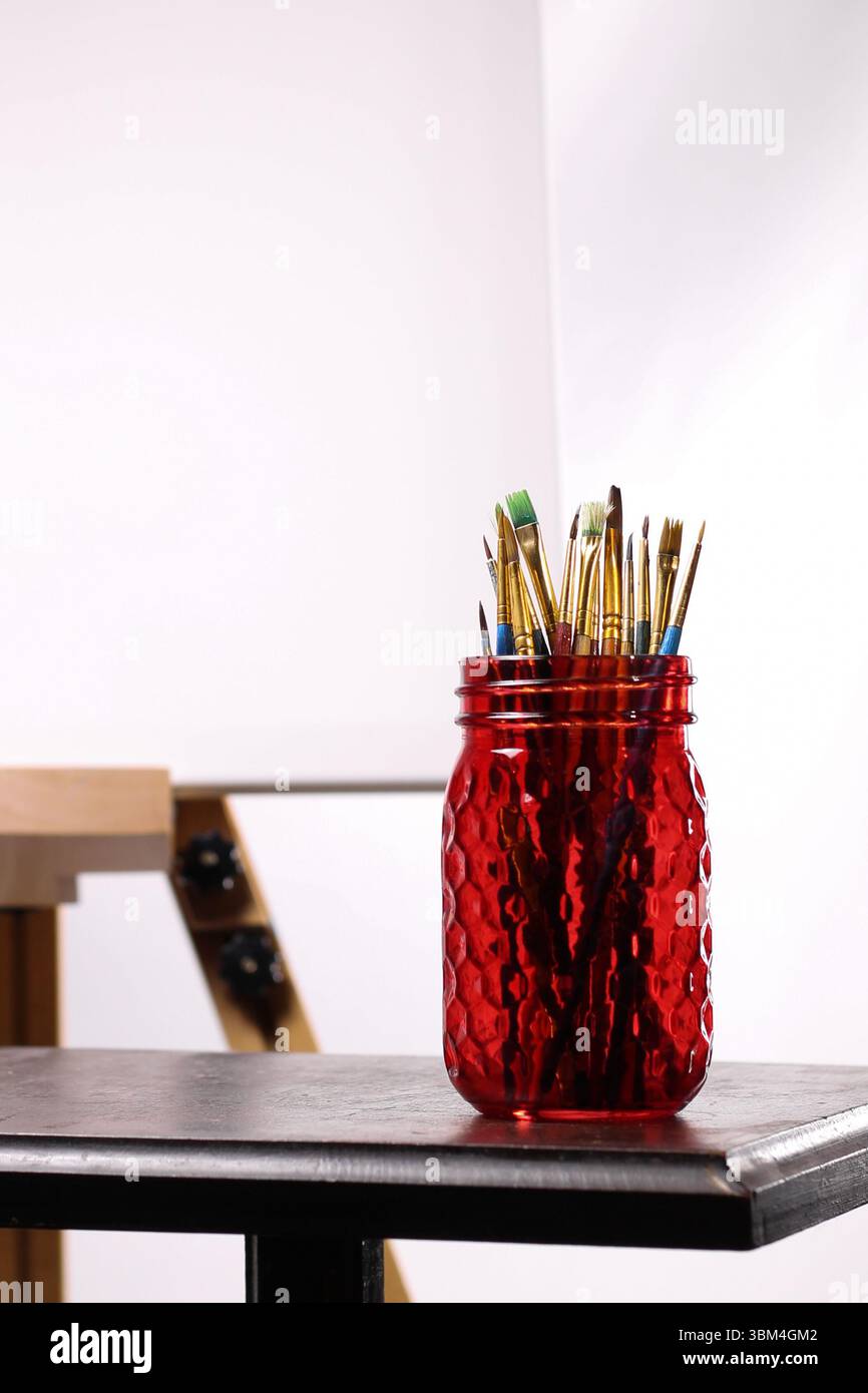 Red Mason pot de pinceaux devant Blank Canvas – Artistic Workspace Still Life Banque D'Images Red Mason pot de pinceaux devant Blank Canvas – Artistic Workspace Still Life Banque D'Images