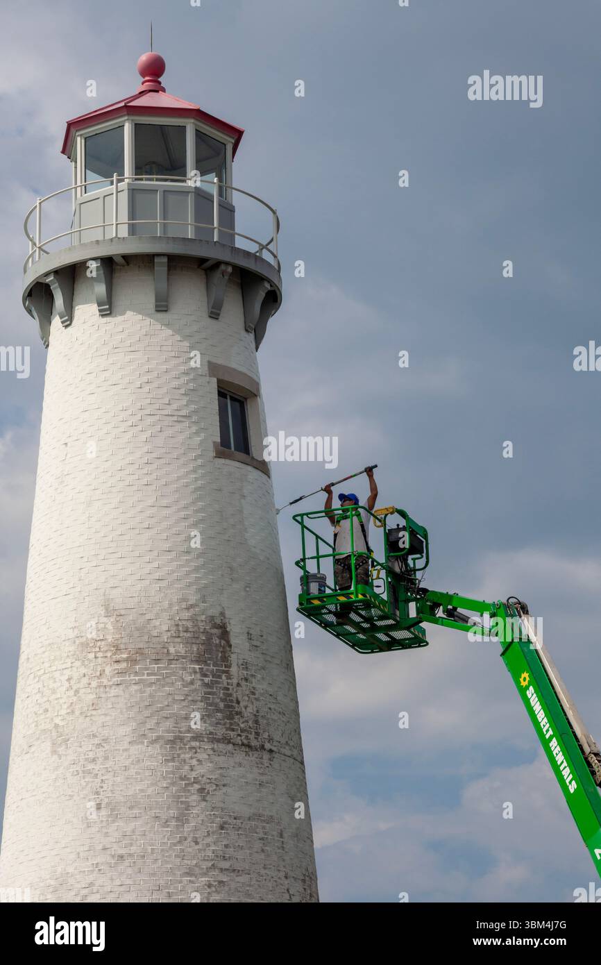 Detroit, Michigan - Un travailleur sur un ascenseur peint le phare du parc d'État de Milliken. Le phare est situé sur la rivière Détroit, près du centre-ville de Détroit. Banque D'Images