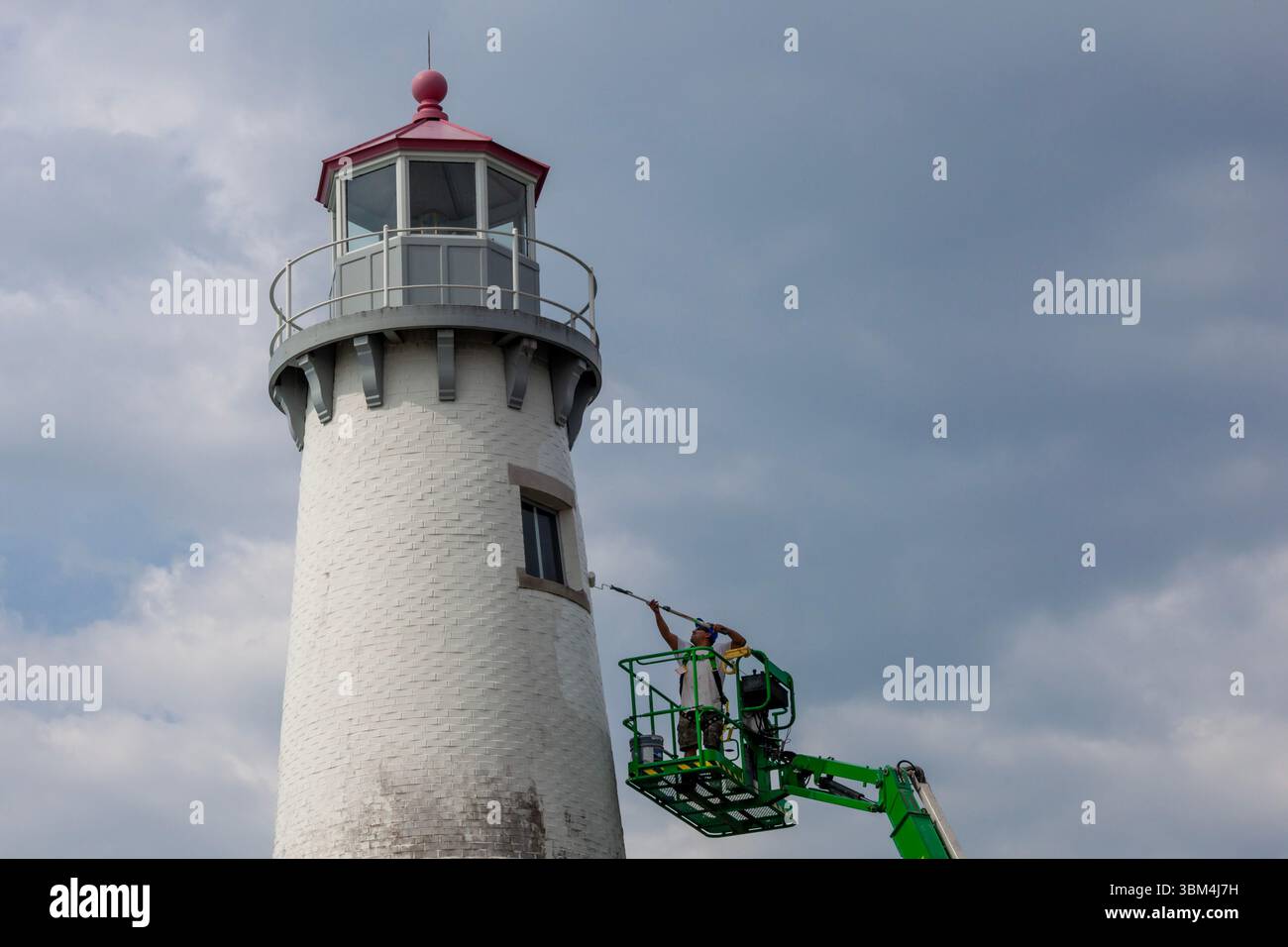 Detroit, Michigan - Un travailleur sur un ascenseur peint le phare du parc d'État de Milliken. Le phare est situé sur la rivière Détroit, près du centre-ville de Détroit. Banque D'Images