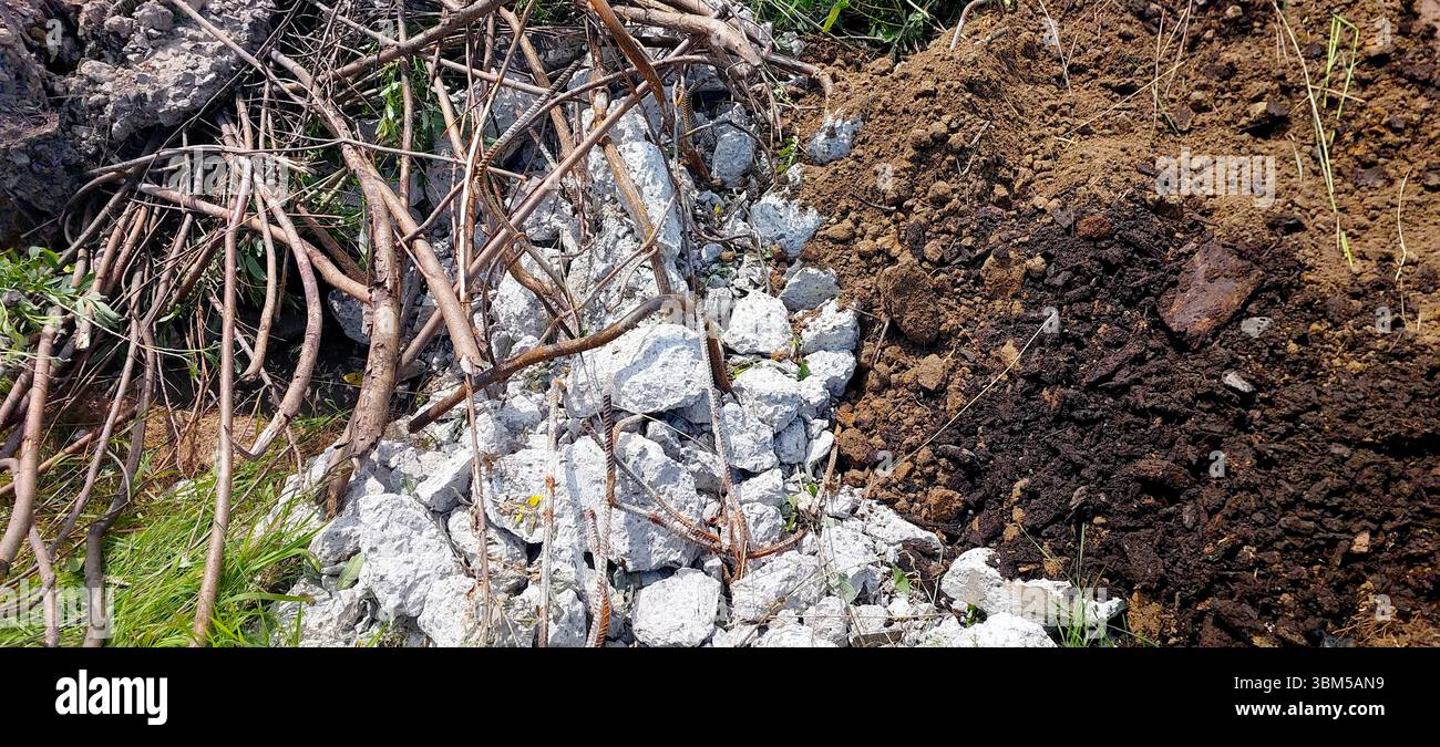 Les débris de construction se trouvent sur le sol d'un chantier, avec de grosses pierres et de la terre le long de branches dispersées et d'herbe. La zone présente des signes de Banque D'Images