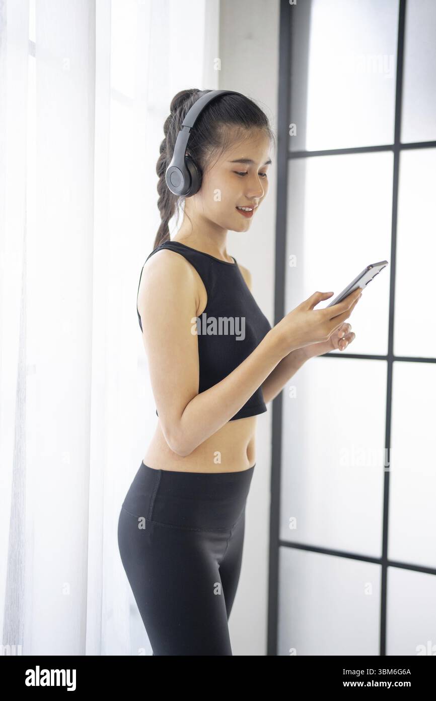 Femme asiatique de fitness utilisant un téléphone intelligent et des écouteurs apprécient écouter de la musique. Femme avec casque smartphone après l'entraînement Banque D'Images