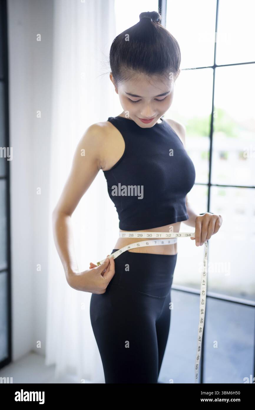Femme asiatique en bonne santé suivant un régime de perte de poids. Femme mince mesurant la taille avec ruban à mesurer après le régime au contrôle du poids à la maison Banque D'Images