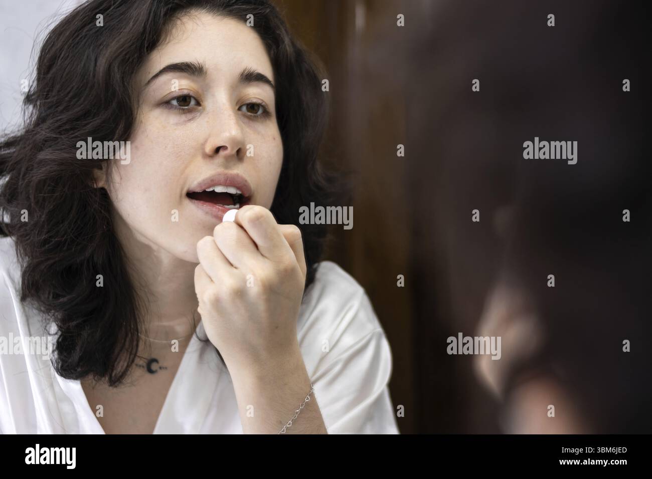 Portrait d'une jeune femme latine appliquant du baume à lèvres ou de la vaseline sur ses lèvres devant le miroir de la salle de bain à la maison. hydrater les lèvres est très impor Banque D'Images