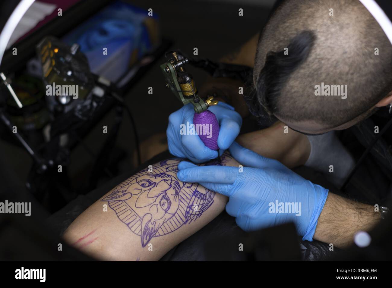 Vue de dessus de tatoueur tatouage une jambe d'une jeune femme étirée sur une civière dans un studio de tatouage Banque D'Images