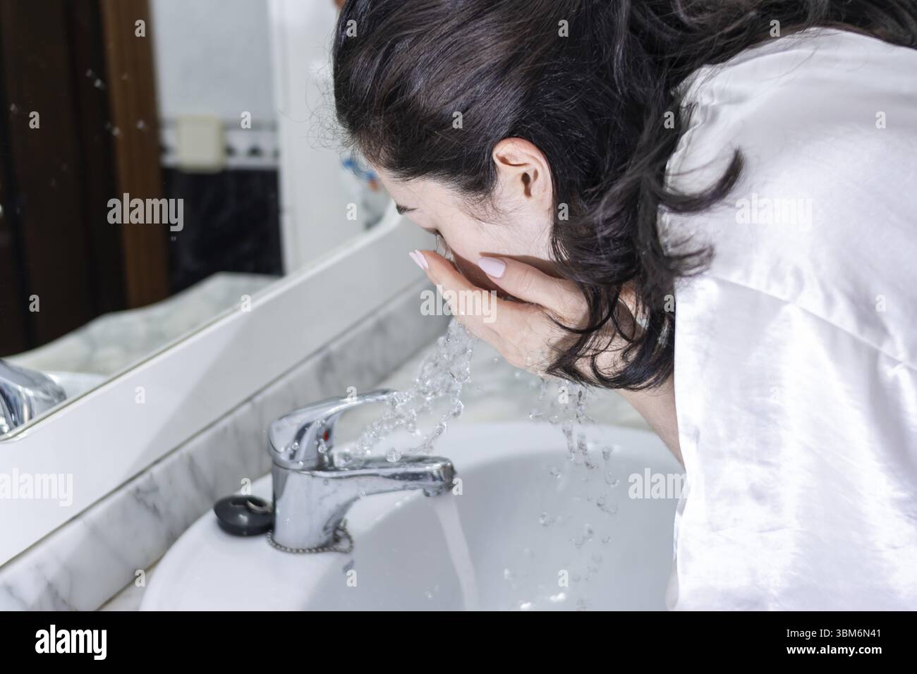 Femme se lavant le visage au lavabo de la salle de bain. Personne se lavant le visage le matin Banque D'Images