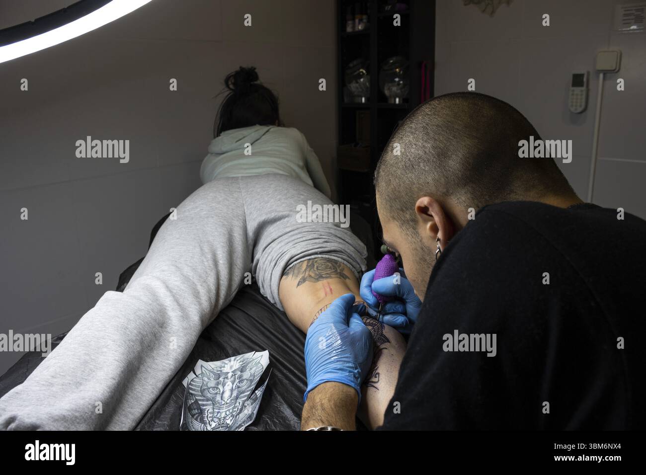 Tatoueur tatouage la jambe d'une jeune femme étirée sur une civière dans un studio de tatouage Banque D'Images