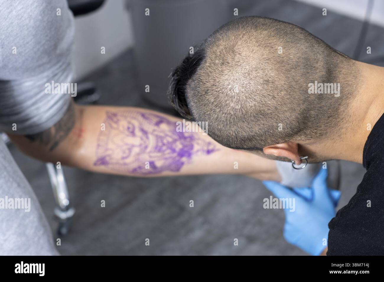 Portrait d'un tatoueur alternatif marquant et perfectionnant le croquis d'un tatouage sur la jambe d'un client avant le tatouage Banque D'Images