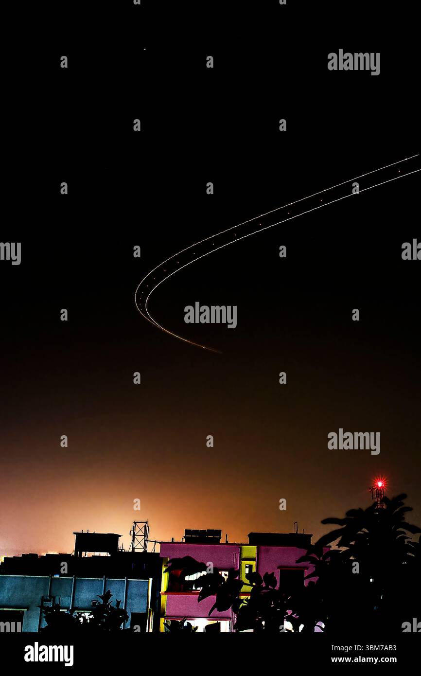 Une superbe photographie de nuit à exposition longue capturant la traînée de lumière incurvée d'un avion survolant un paysage urbain vibrant. Banque D'Images