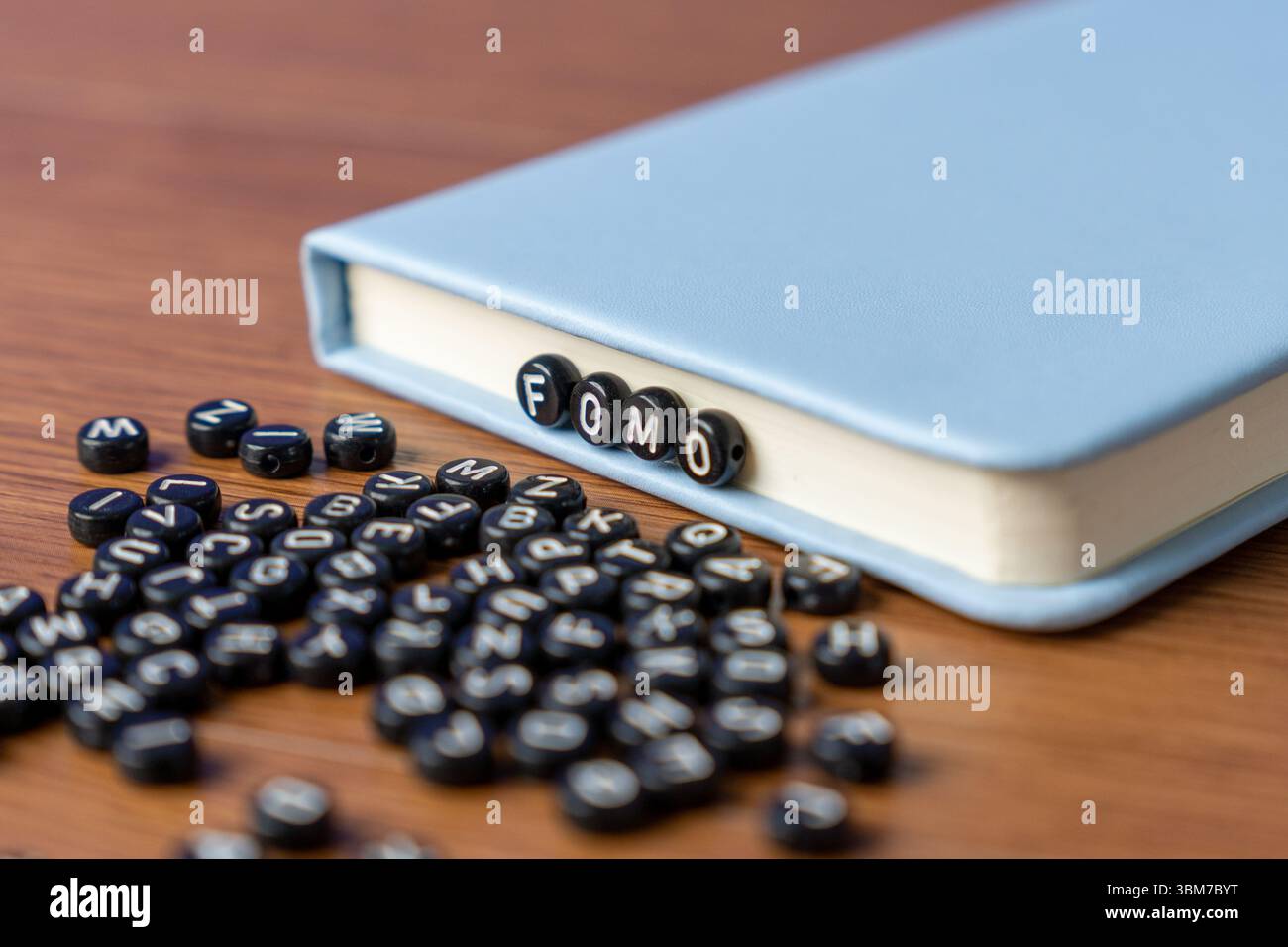 Perles alphabet orthographiant 'FOMO' avec des perles plus dispersées sur une table en bois. Peur de manquer, anxiété sociale et concept de santé mentale. Banque D'Images
