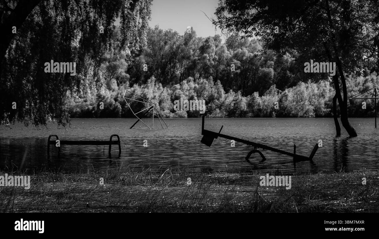 Une image en noir et blanc d’un terrain de jeu partiellement sous l’eau, évoquant un sentiment de désolation et d’abandon. Banque D'Images
