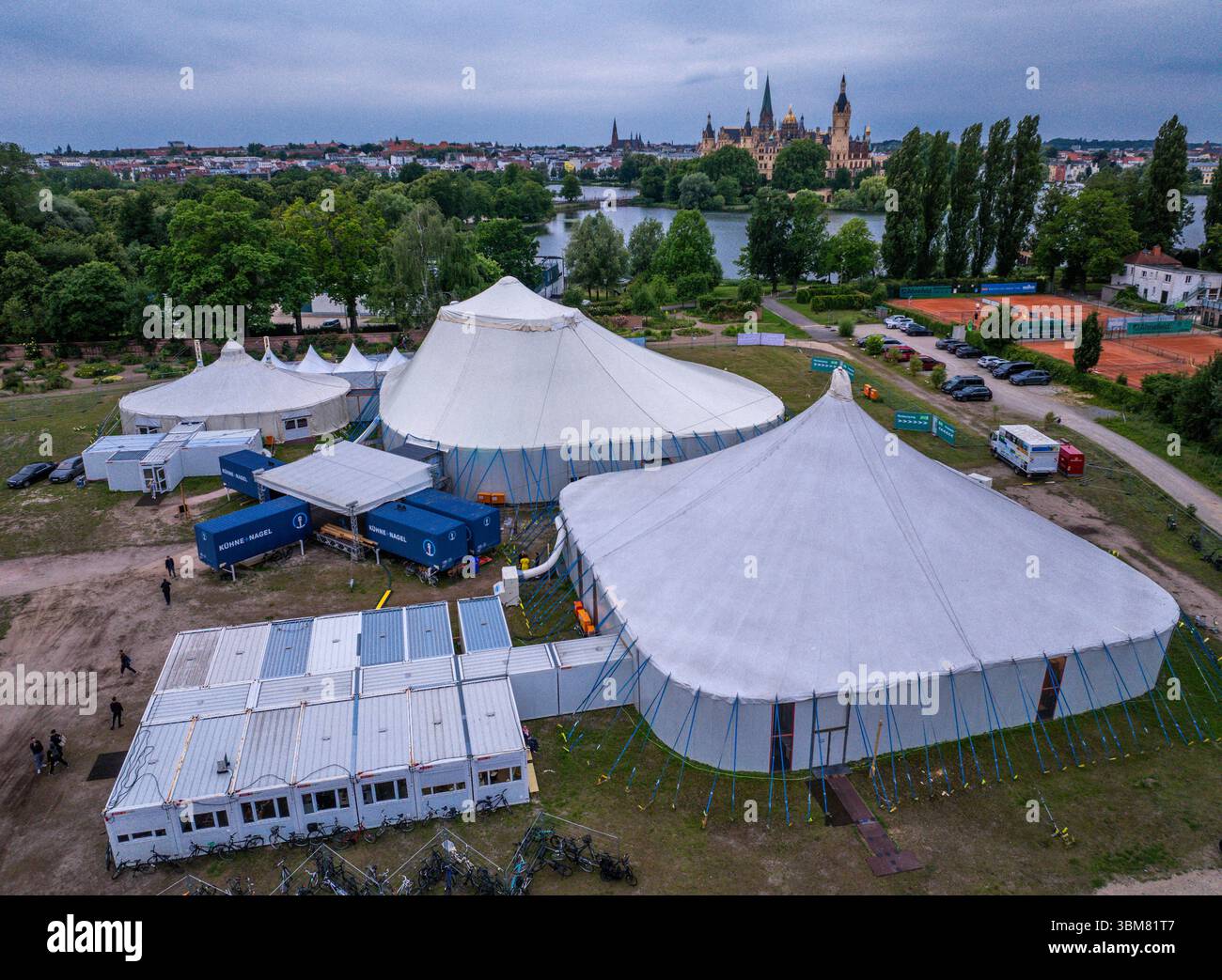 Schwerin, Allemagne. 24 juin 2025. Les acteurs, musiciens et techniciens du Théâtre d'État de Mecklembourg travaillent dans trois tentes et conteneurs spéciaux et répètent pour l'opérette 'la veuve joyeuse'. (Vue aérienne avec un drone). En raison de travaux de construction importants dans le bâtiment historique de la scène, six productions sont prévues pour la saison 2025/2026 dans la tente de théâtre sur le lac Schwerin. En plus des pièces de théâtre, ballets, opéras et opérettes, l'Orchestre d'État de Mecklembourg jouera également ses concerts dans la tente. Crédit : Jens Büttner/dpa/Alamy Live News Banque D'Images