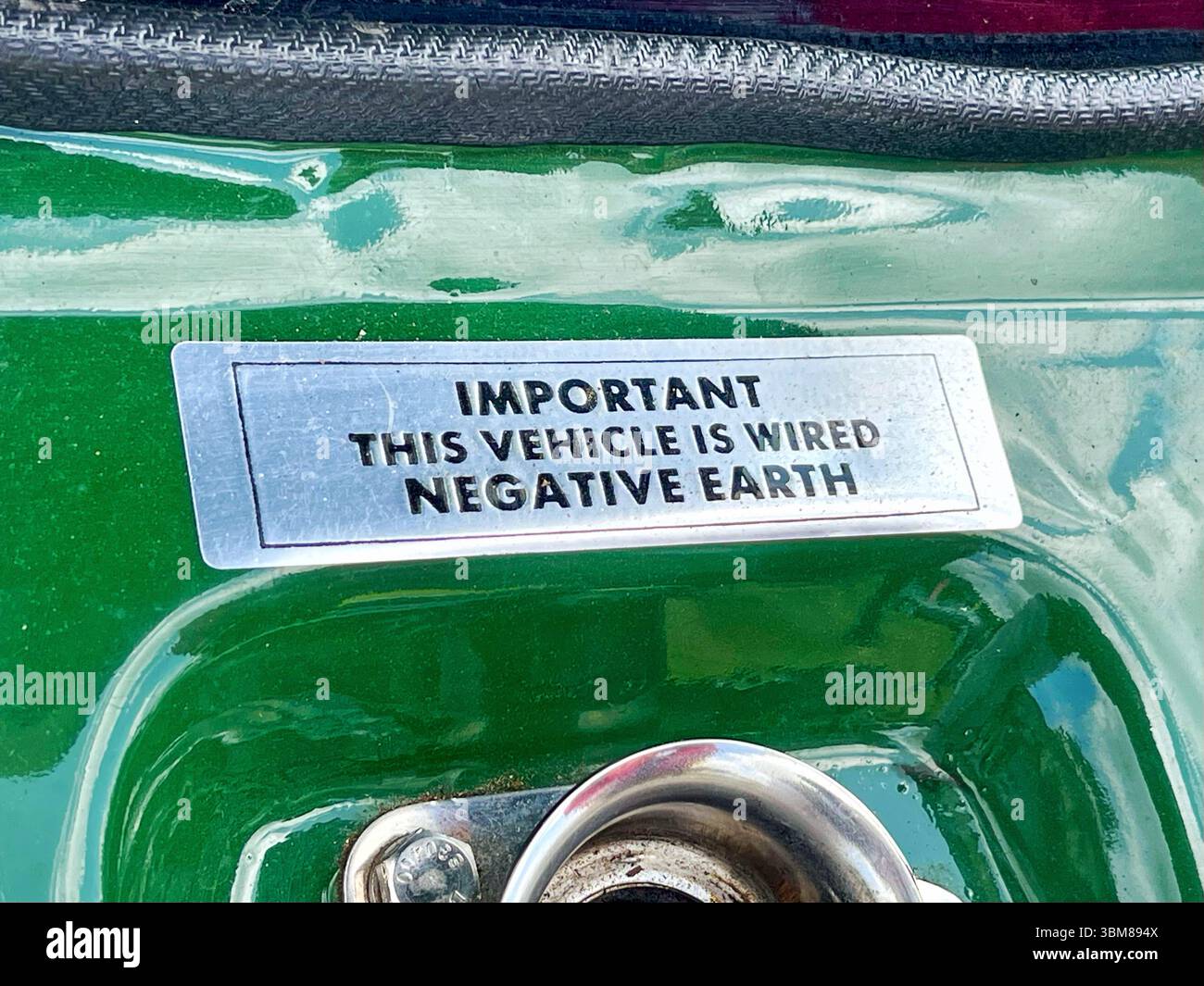 La plaque d'identification en métal sur le châssis peint en vert indique « masse négative », marquant le système électrique mis à la terre de la voiture - détail automobile de voiture classique Banque D'Images