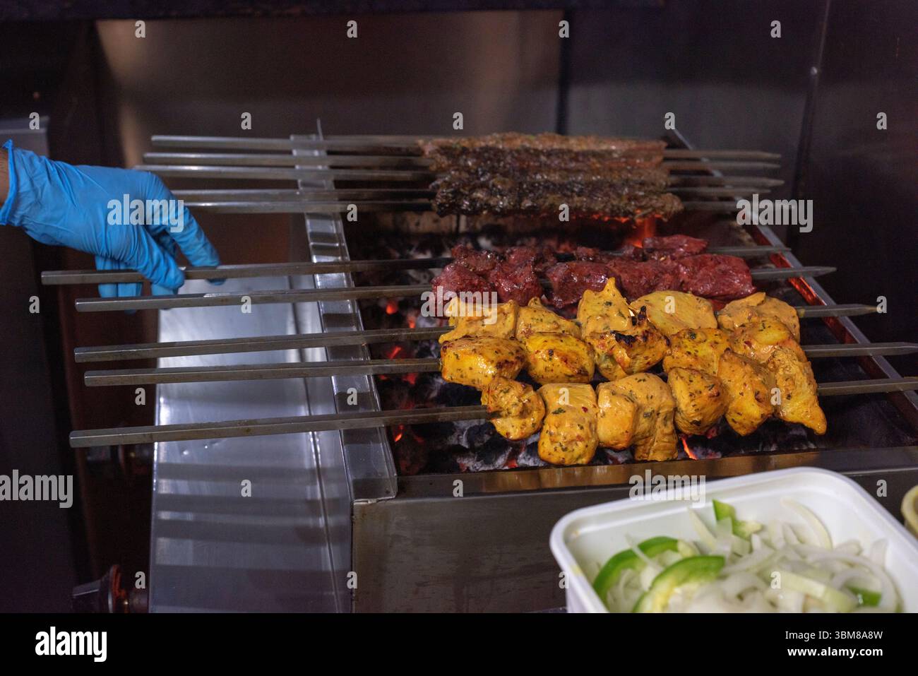 Flammes du gril et main gantée bleue du chef tournant les kebabs Banque D'Images