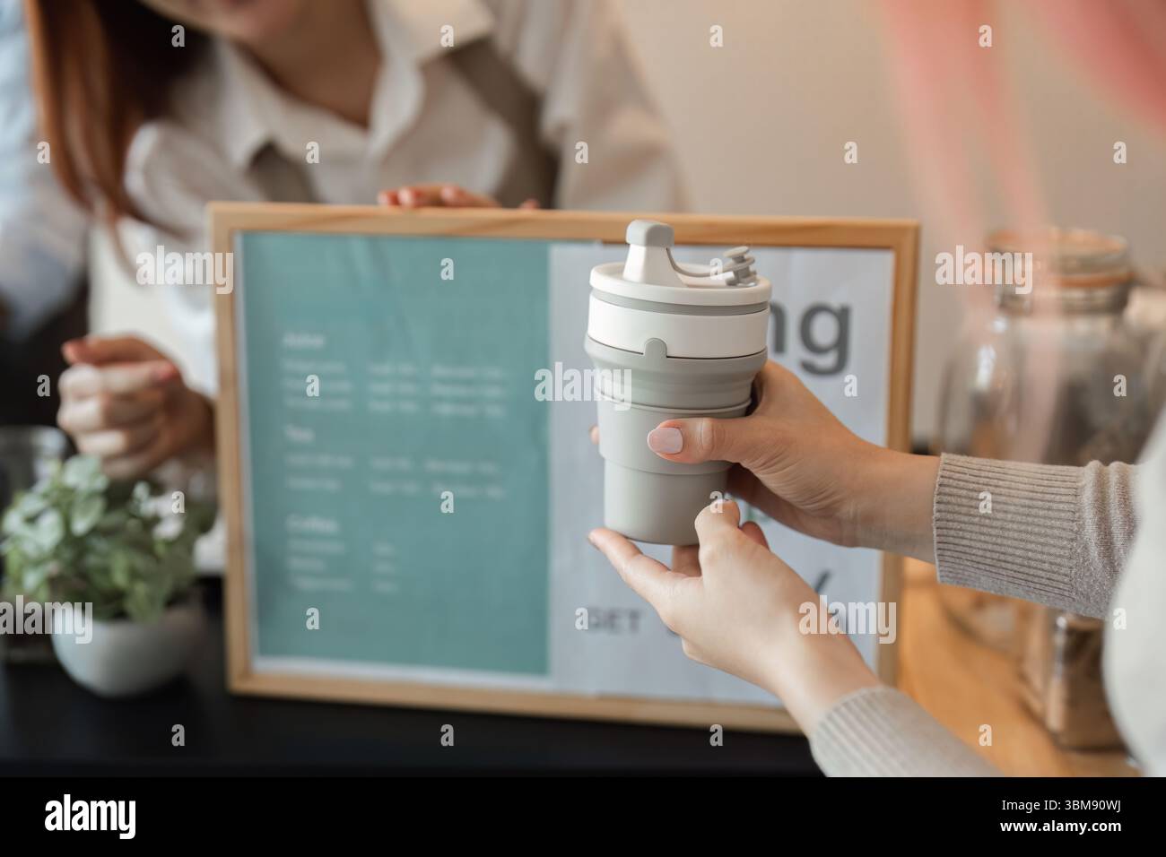 Durabilité et responsabilité personnelle. Un client tient fièrement un gobelet réutilisable tout en discutant avec un barista pour promouvoir des pratiques écologiques. Banque D'Images