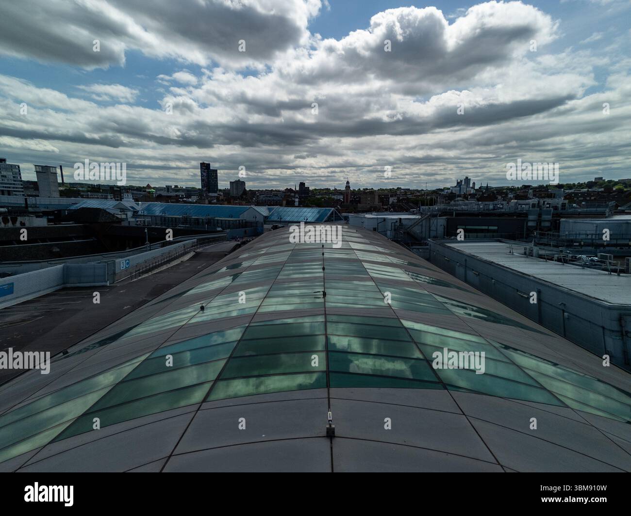 Toit en verre moderne reflétant le ciel nuageux, surplombant le paysage urbain avec des bâtiments industriels et des zones commerciales Banque D'Images