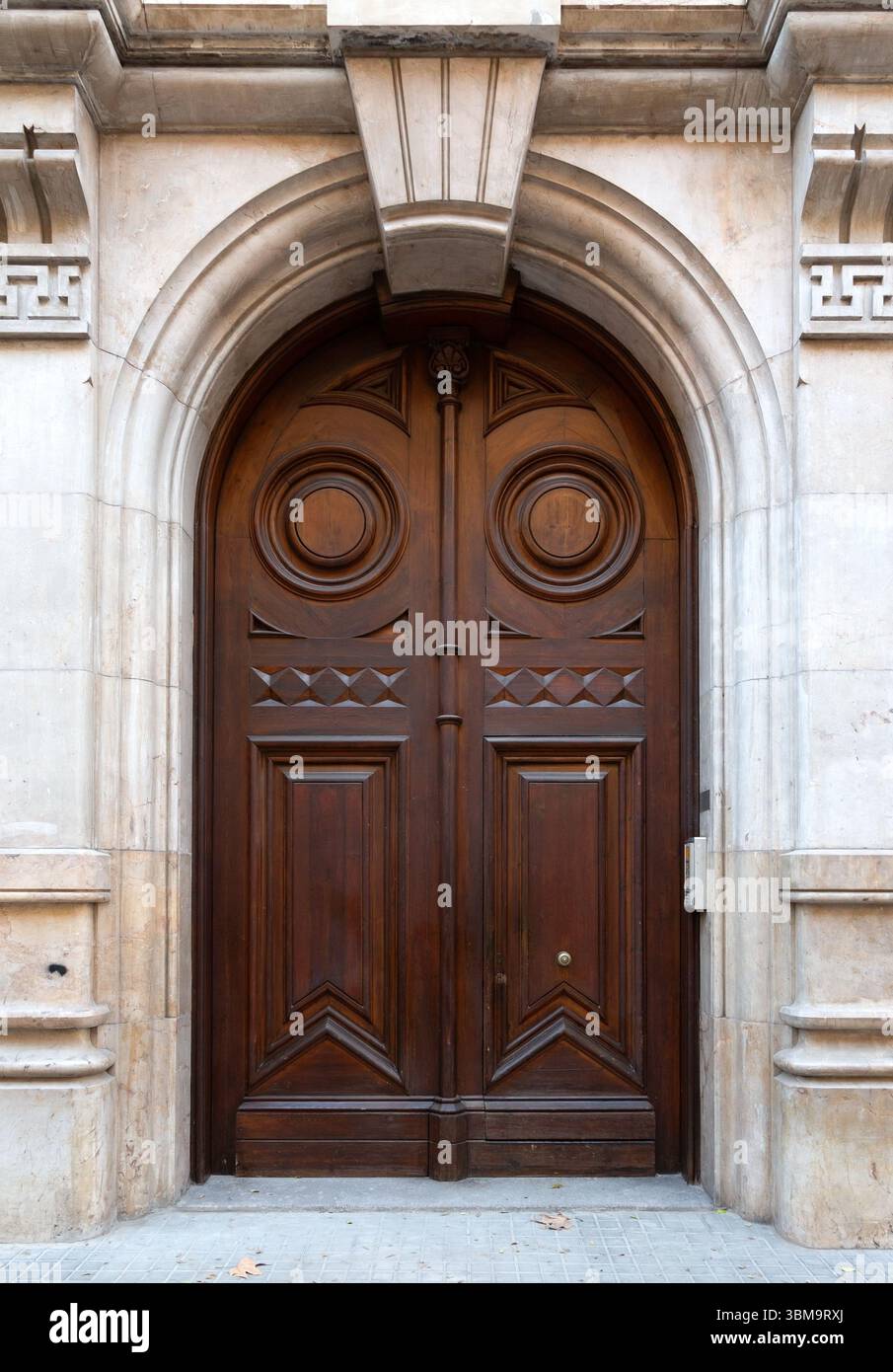 Double porte classique en bois avec sculptures complexes, sertie dans une arche en pierre, ajoutant une touche d'élégance et d'histoire à la façade d'un bâtiment Banque D'Images