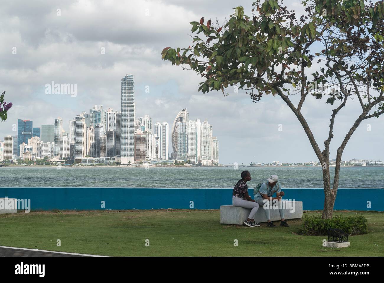 Un couple assis à l'ombre d'un arbre dans un parc. Skyline du cty en arrière-plan. Panama City, Panama. Banque D'Images