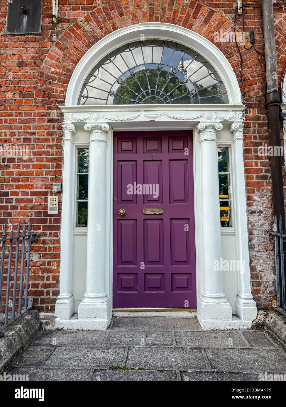 Vitrine géorgienne à Dublin avec une porte violette vibrante, une fenêtre décorative avec lumière en éventail, des colonnes blanches et une façade de bâtiment en briques rouges. Banque D'Images