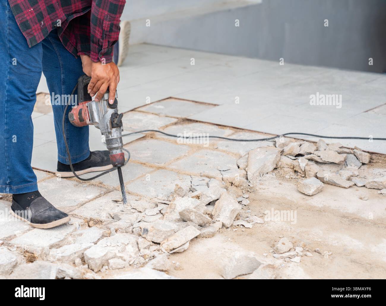 Le travailleur démolit la vieille surface de béton carrelée avec un marteau-piqueur. Banque D'Images